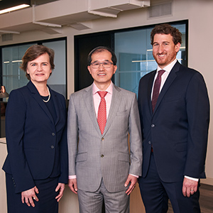 Three people in business attire, one woman and two men, stand for a photo in new office space.